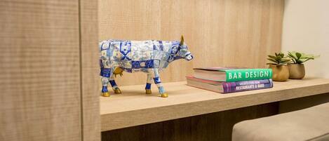 Una estantería con una figurita de toro azul y blanco, una pila de libros con el título 'BAR DESIGN' y dos pequeñas macetas con plantas.
