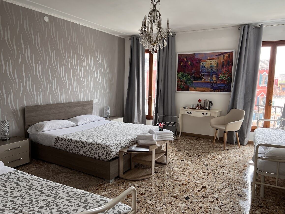 Quarto de hotel com cama, mesa de cabeceira, escrivaninha, cadeira e um quadro na parede.