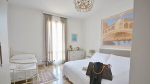 A hotel room with a bed, a chair, a nightstand, a lamp, a painting, and a window with curtains.