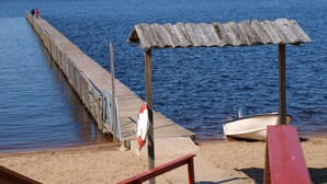 A wooden pier extending into calm waters, a lifebuoy attached to the pier, and a small boat docked nearby. - Årsunda Strandbad (Arsunda)