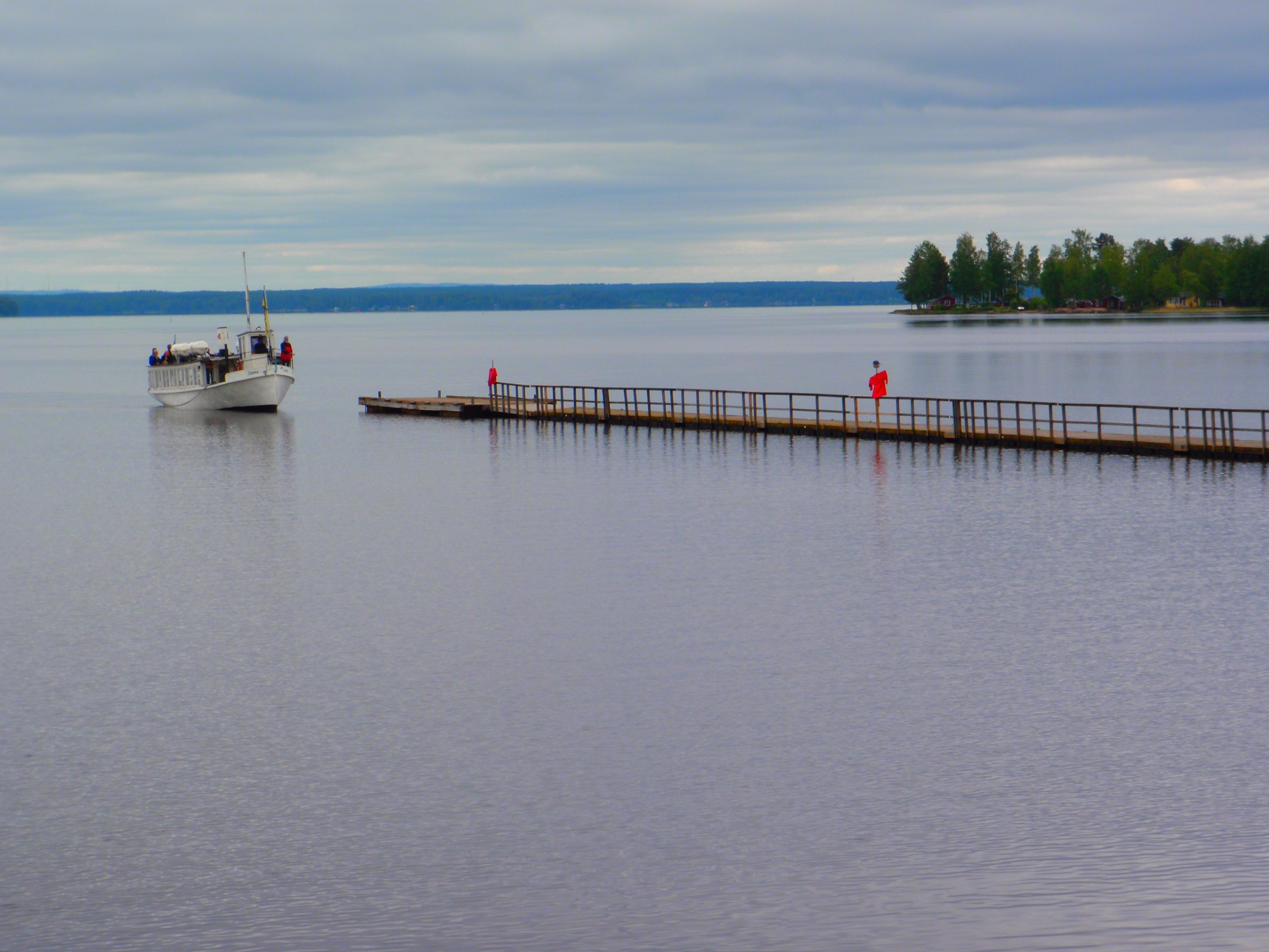 A calm lake with a boat docked on the left and a wooden pier extending into the water.