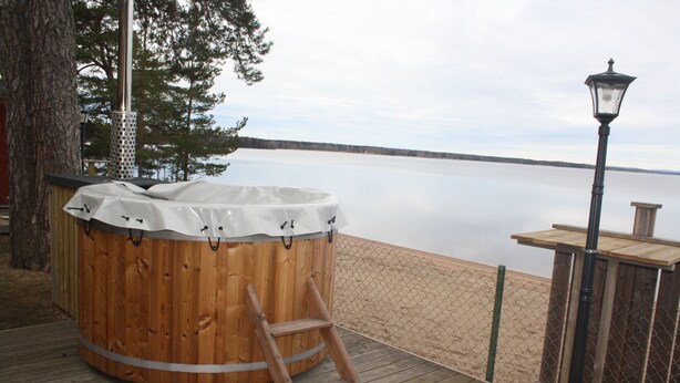 A wooden hot tub on a deck with a ladder, overlooking a calm body of water. - Årsunda Strandbad (Arsunda)