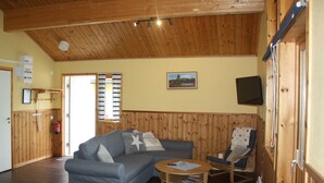 A cozy living room with a wooden ceiling, a grey sofa, a rocking chair, and a small table. - Årsunda Strandbad (Arsunda)