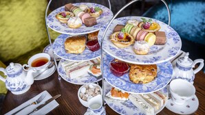 A tiered tea service with various pastries and sandwiches, accompanied by teacups and a teapot.