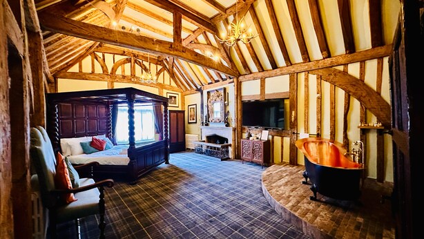 A room with a four-poster bed, a fireplace, a television, and a wooden ceiling.