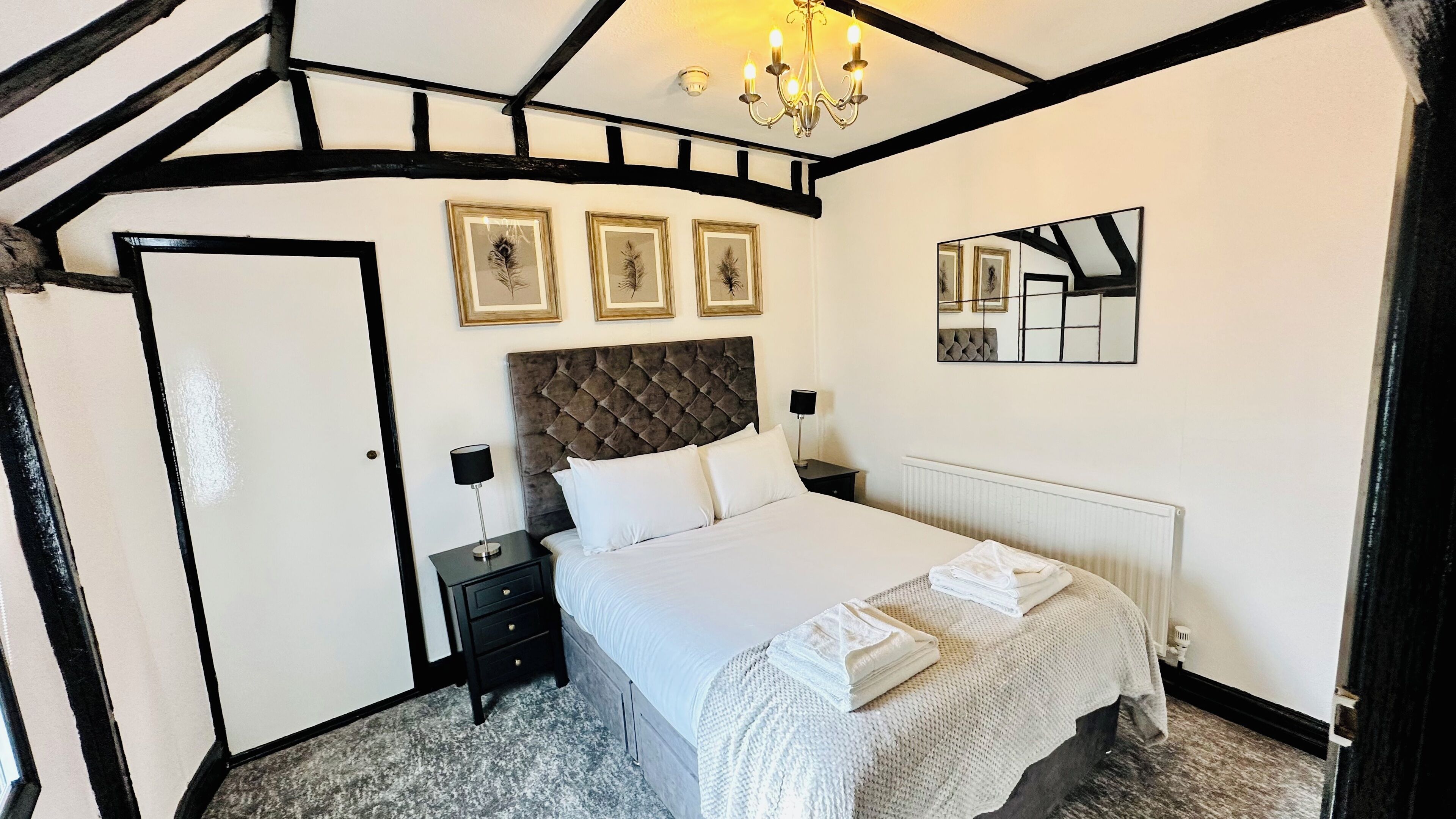 Quarto com cama grande, cômoda, mesa de cabeceira, lustre e três quadros na parede.