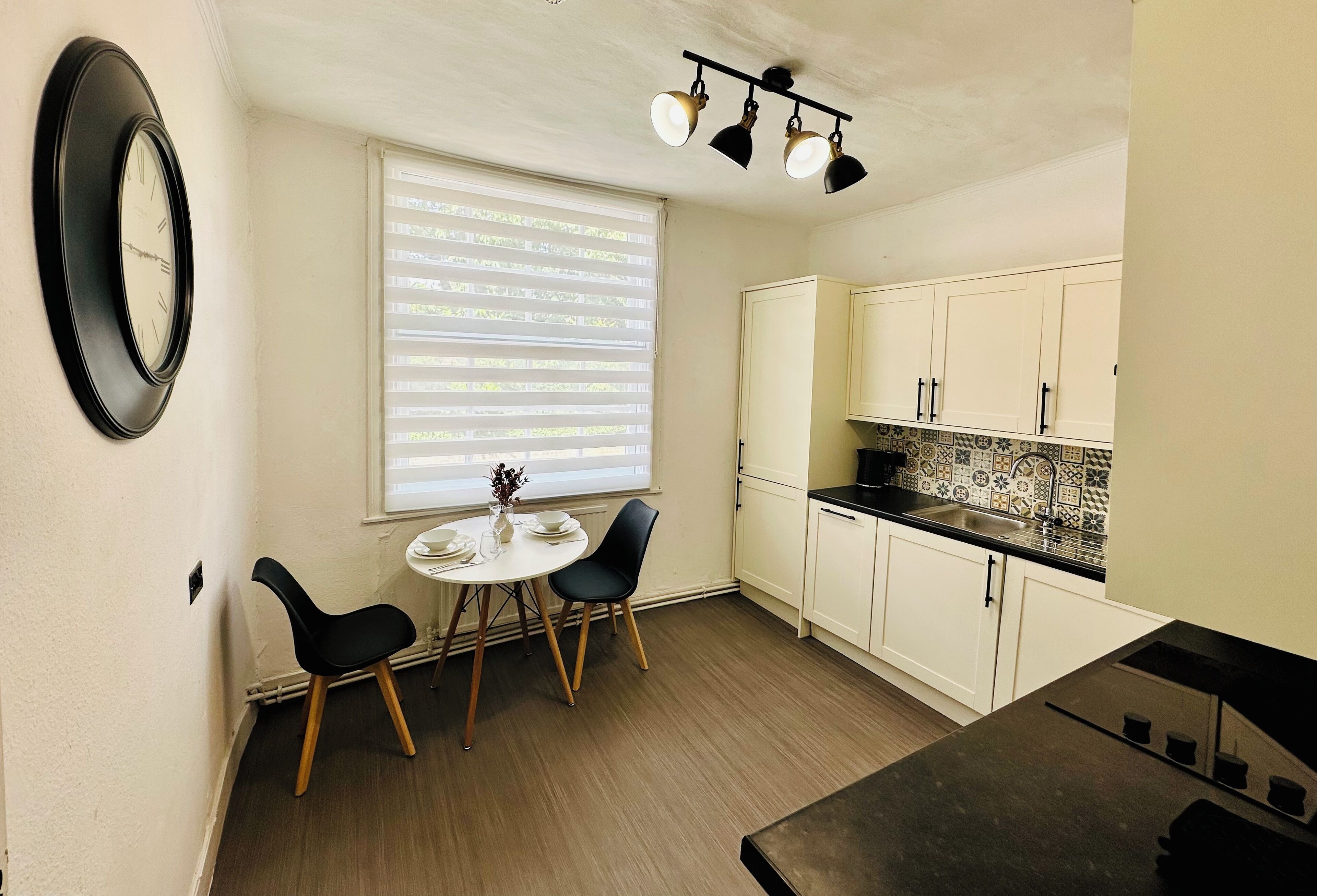 A compact kitchen with white cabinets, a black countertop, and a dining area with two chairs and a small table.