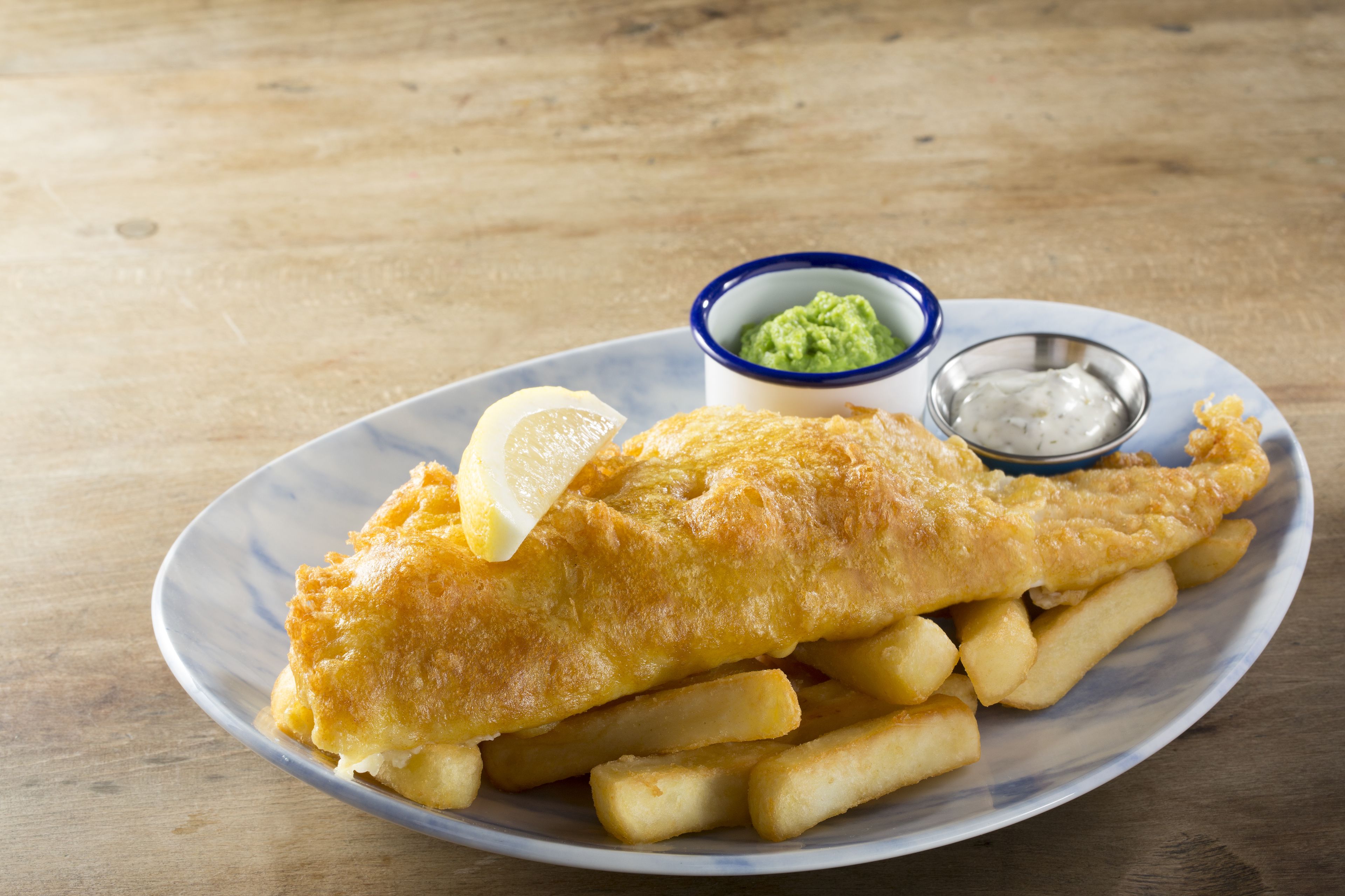 A plate of fish and chips with lemon wedges and two dipping sauces.
