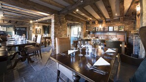 A restaurant with exposed wooden beams, brick walls, and a long dining table set for a meal.