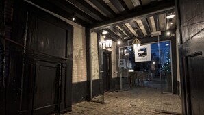 A cobblestone entrance to a building with a glass door, a sign reading "The Ostrich," and a brick wall.