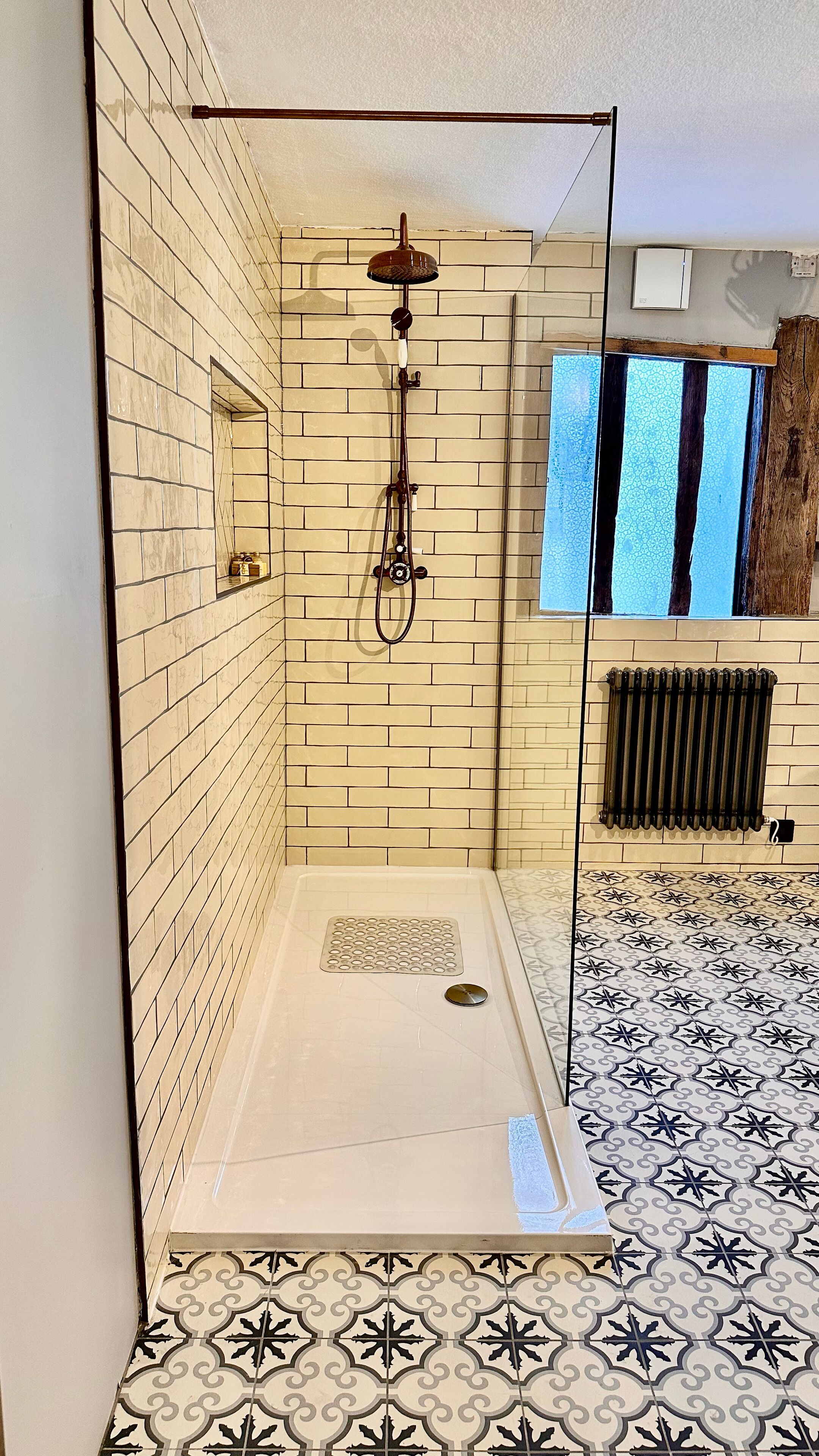 A shower room with a tiled floor, a showerhead, and a radiator.