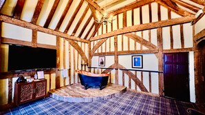 A room with exposed wooden beams, a large bathtub, a television, and a checkered floor.