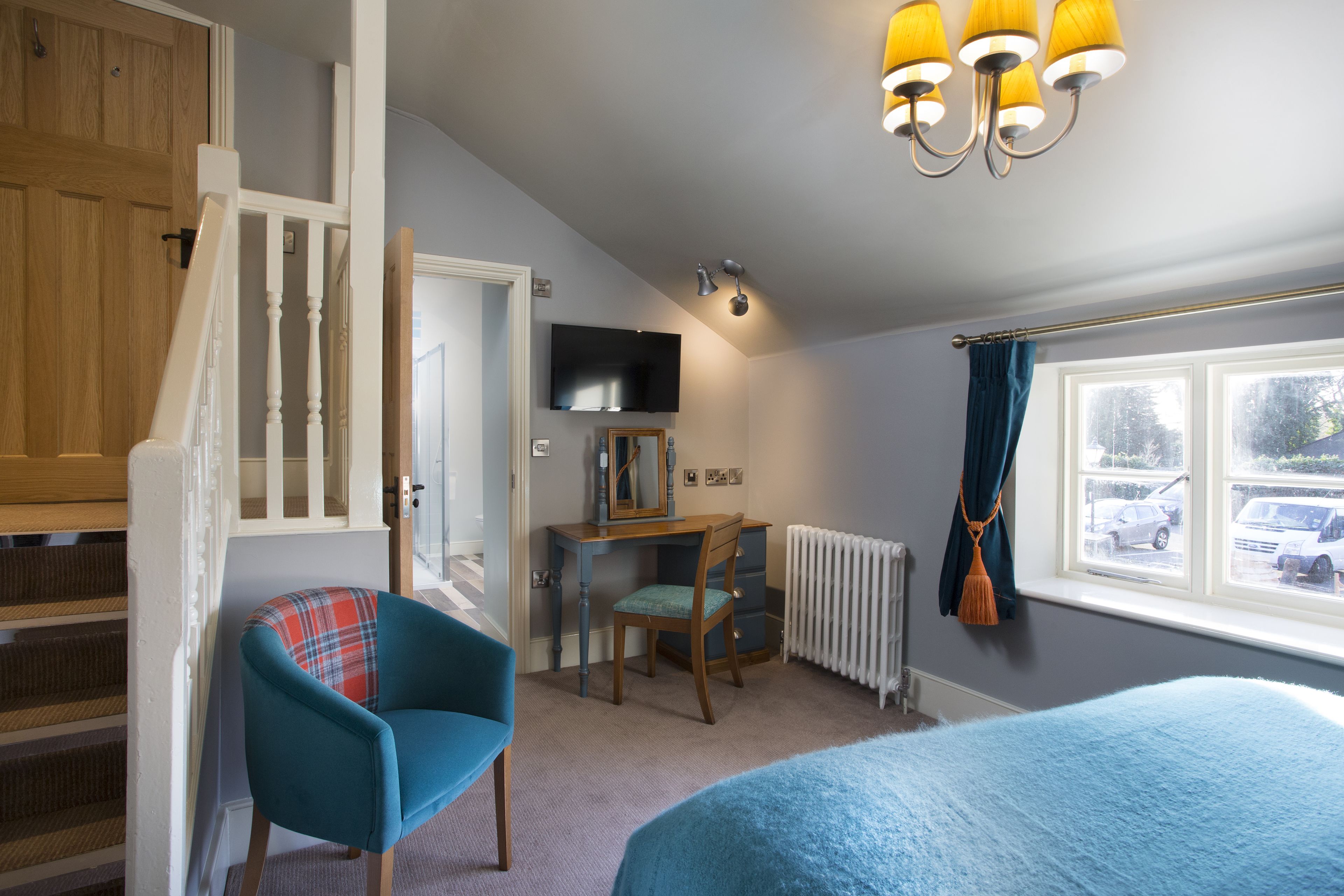 Ein Schlafzimmer mit Bett, Schreibtisch, Stuhl, einem Fenster mit Vorhängen, einer Heizung und einer Treppe.