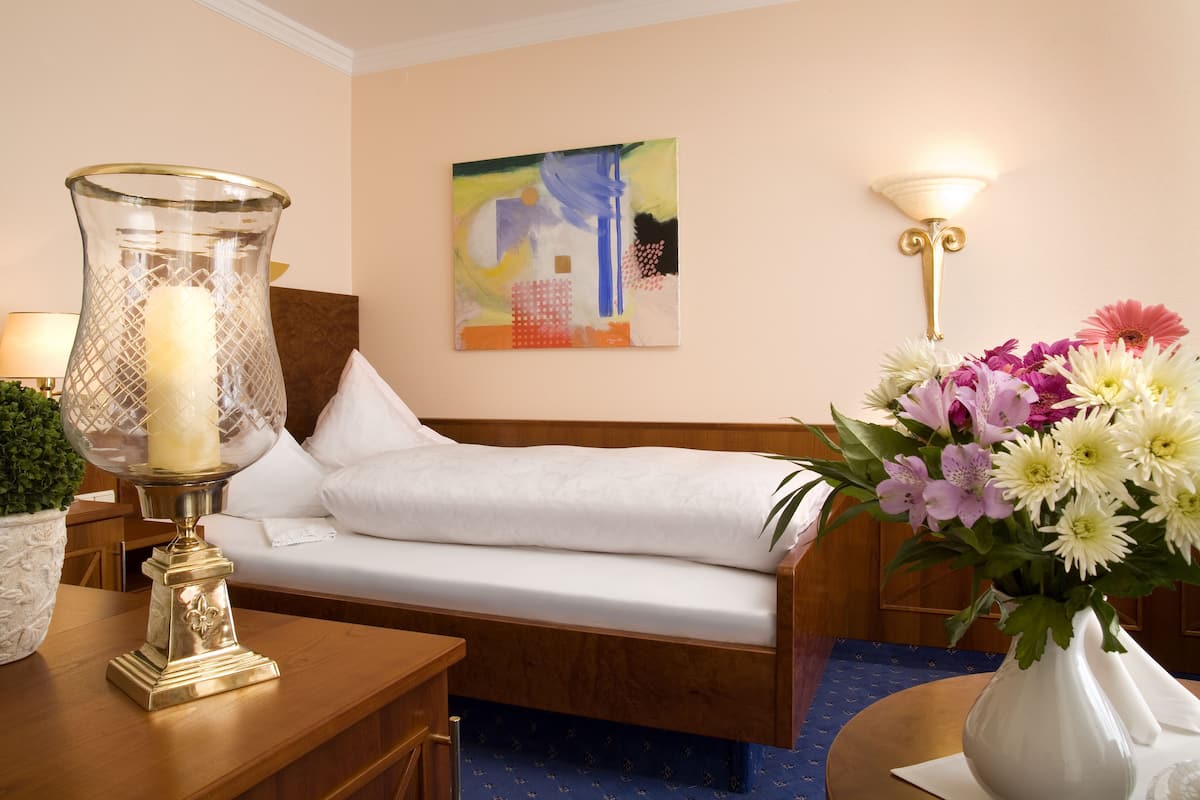 Une chambre d’hôtel avec un lit, une table de chevet avec une lampe, un vase de fleurs et un tableau au mur.