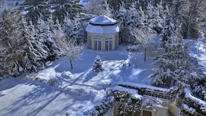 Schneebedeckte Landschaft mit Poolbereich, Laube und umliegenden Bäumen.