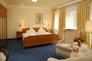 A hotel room with a wooden bed, two bedside tables with lamps, a chair, a small table with a vase of flowers, and a framed picture on the wall. - Hotel & SPA Fontenay (Bad Woerishofen)