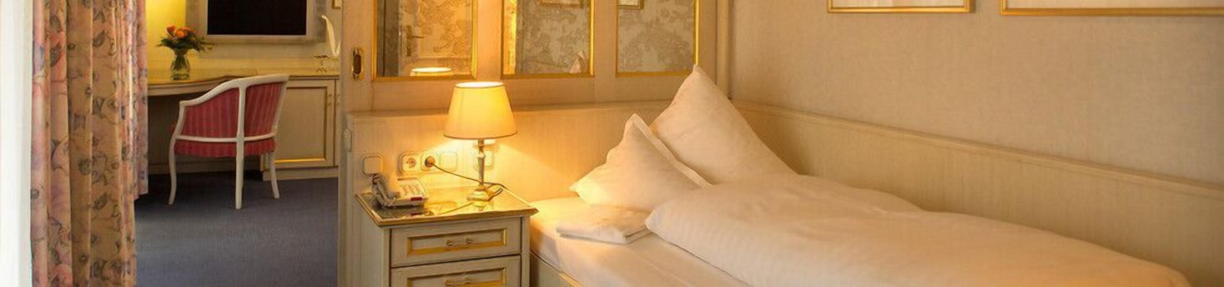 Una habitación de hotel con una cama, una mesita de noche con lámpara, una silla y un escritorio.