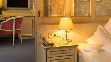 Una habitación de hotel con una cama, una mesita de noche con lámpara, una silla y un escritorio.