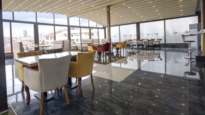 Amplio espacio interior con techos altos, grandes ventanales que ofrecen vistas de la ciudad y una variedad de arreglos de asientos, incluyendo mesas y sillas.