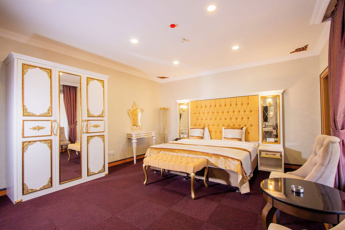 Una habitación de hotel con una cama grande, una zona de estar con una mesa y un armario con detalles dorados.