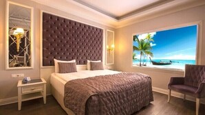 Un dormitorio con una cama grande, una ventana con vista al mar, una mesita de noche y una silla.