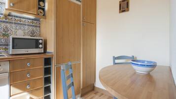 A compact kitchen with a microwave, wooden cabinets, and a dining table with a bowl.