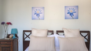 Un dormitori amb llit, dos coixins, una tauleta de nit, una làmpada i dues pintures florals penjades a la paret.