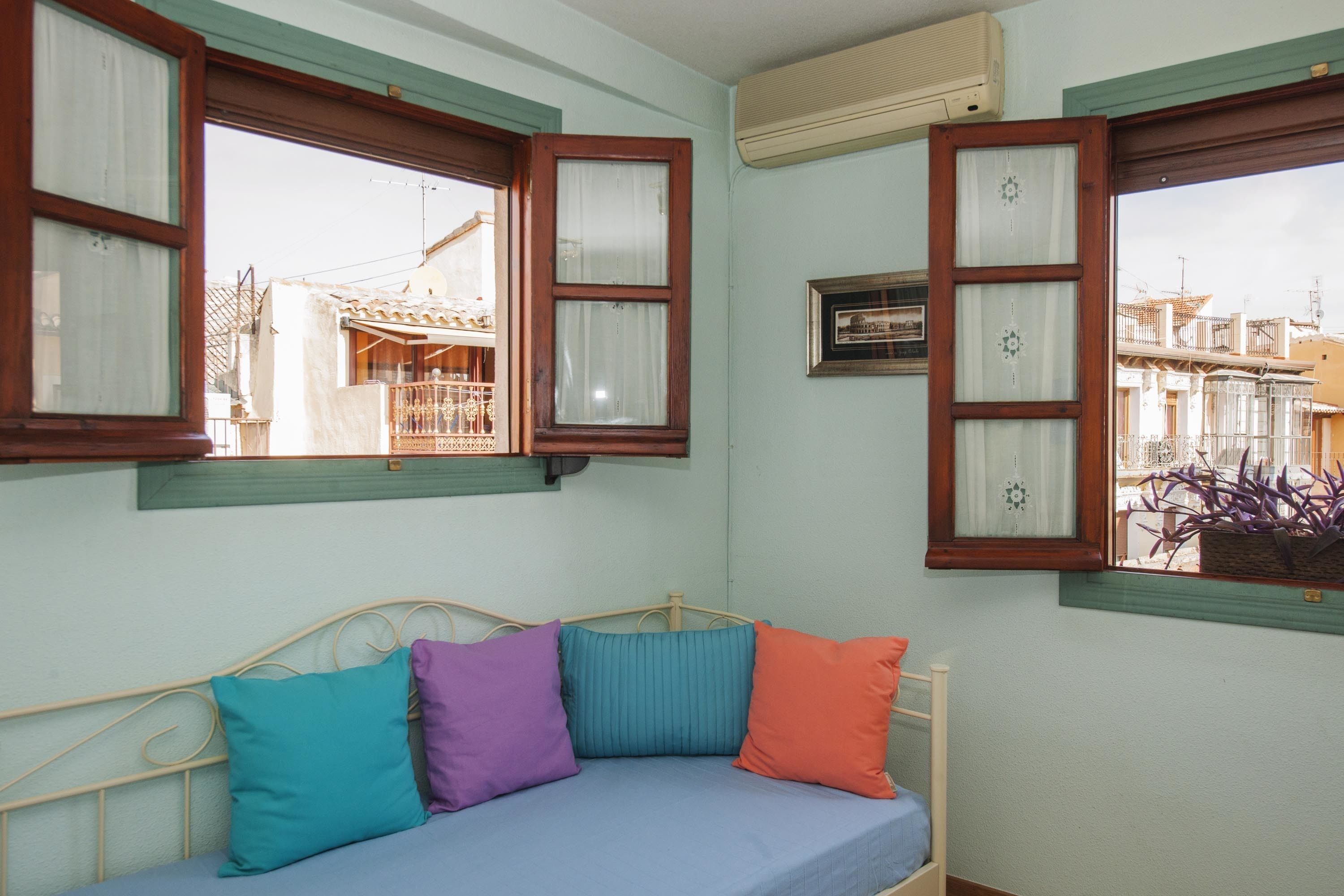 A room with a bed, a window with wooden shutters, and a wall-mounted air conditioner.