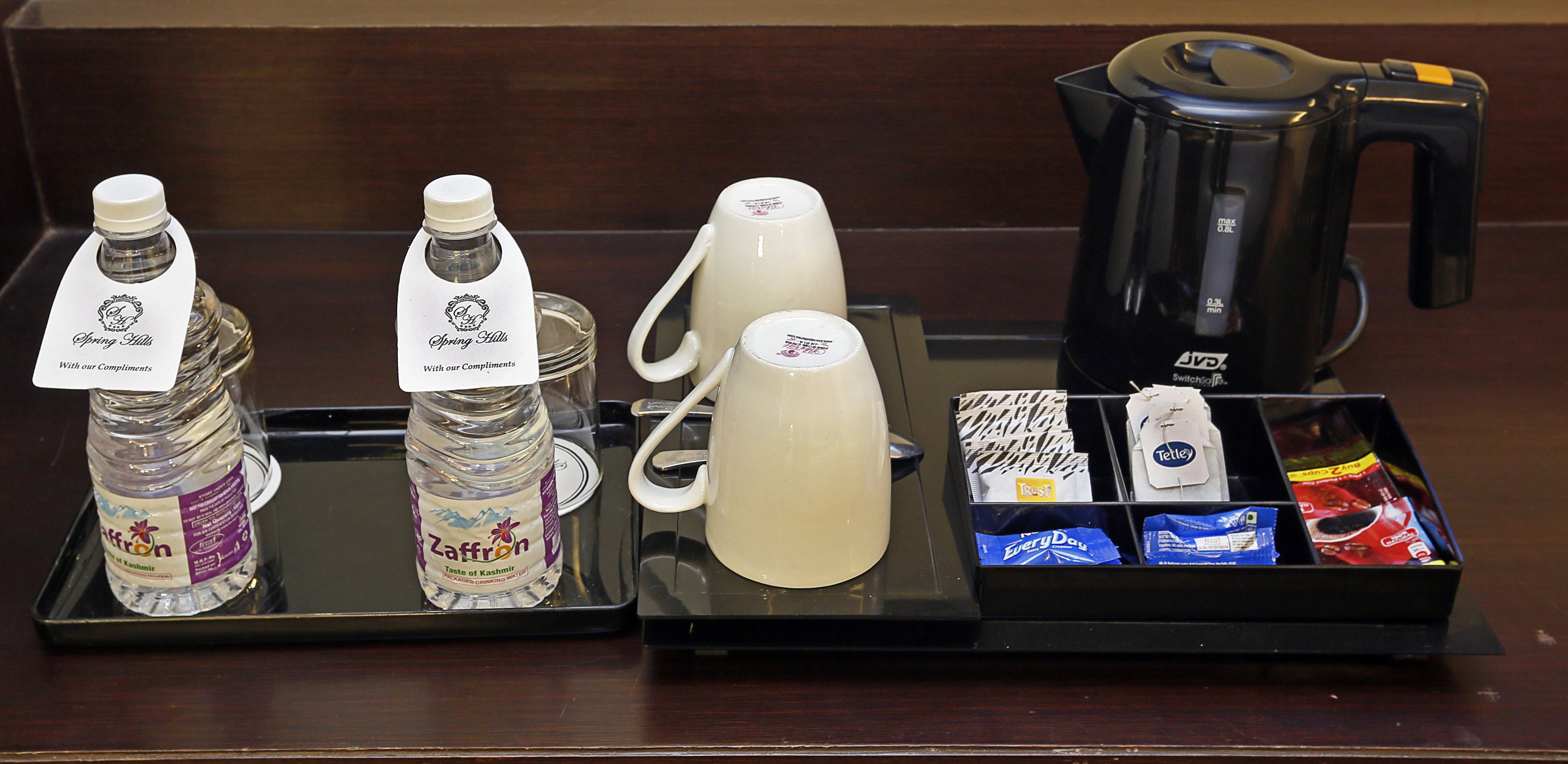 A coffee station with a coffee maker, two water bottles, a mug, and various coffee packets.