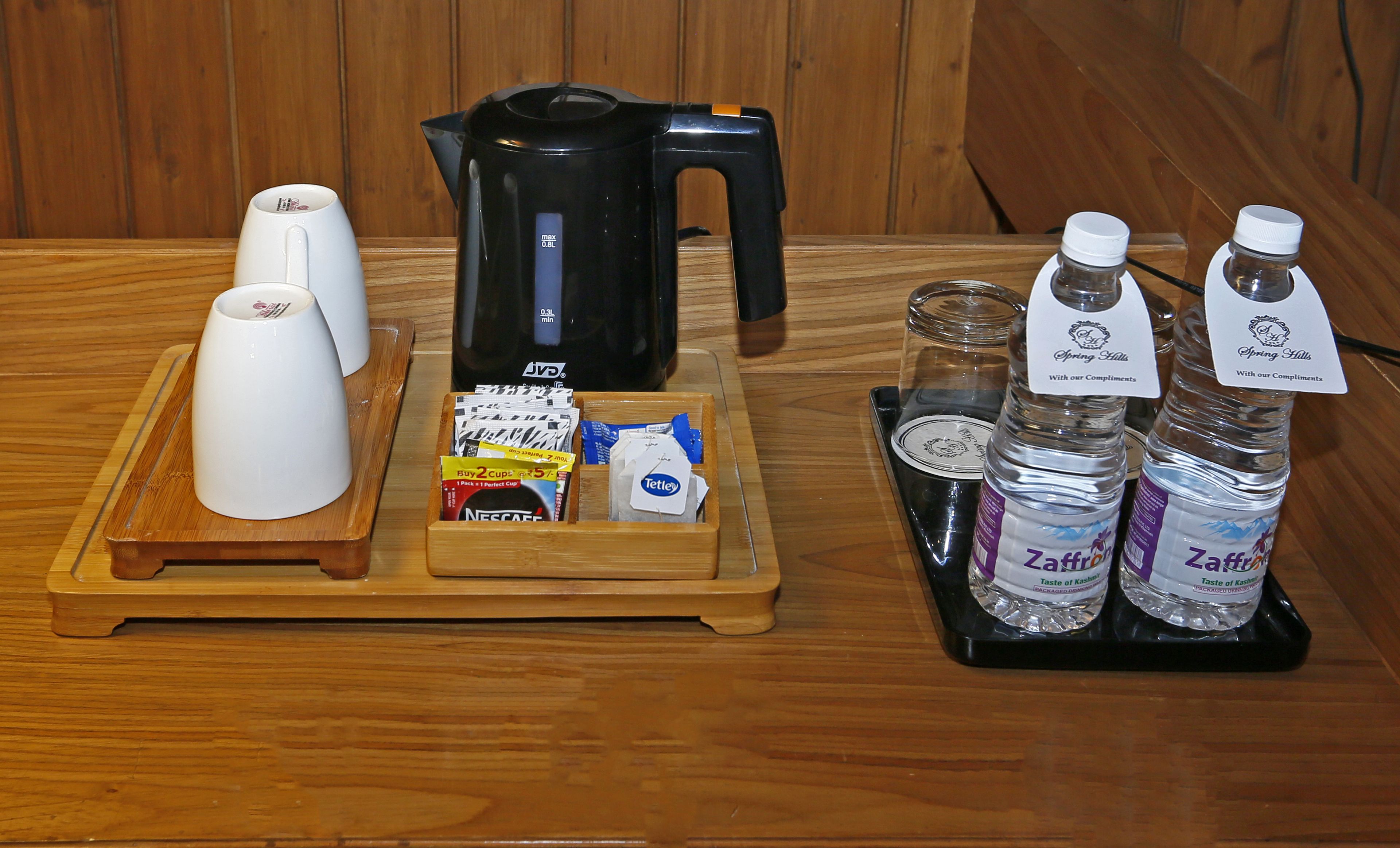 A wooden tray with a coffee maker, a white coffee cup, a box of coffee pods, and two water bottles labeled "Zaffron".