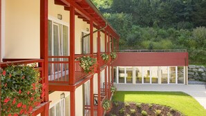 A building with a red balcony and flower boxes, a well-maintained lawn, and a stone wall in the background. - Landhotel Kreinerhof - Self Check In 24h möglich (Lurnfeld)