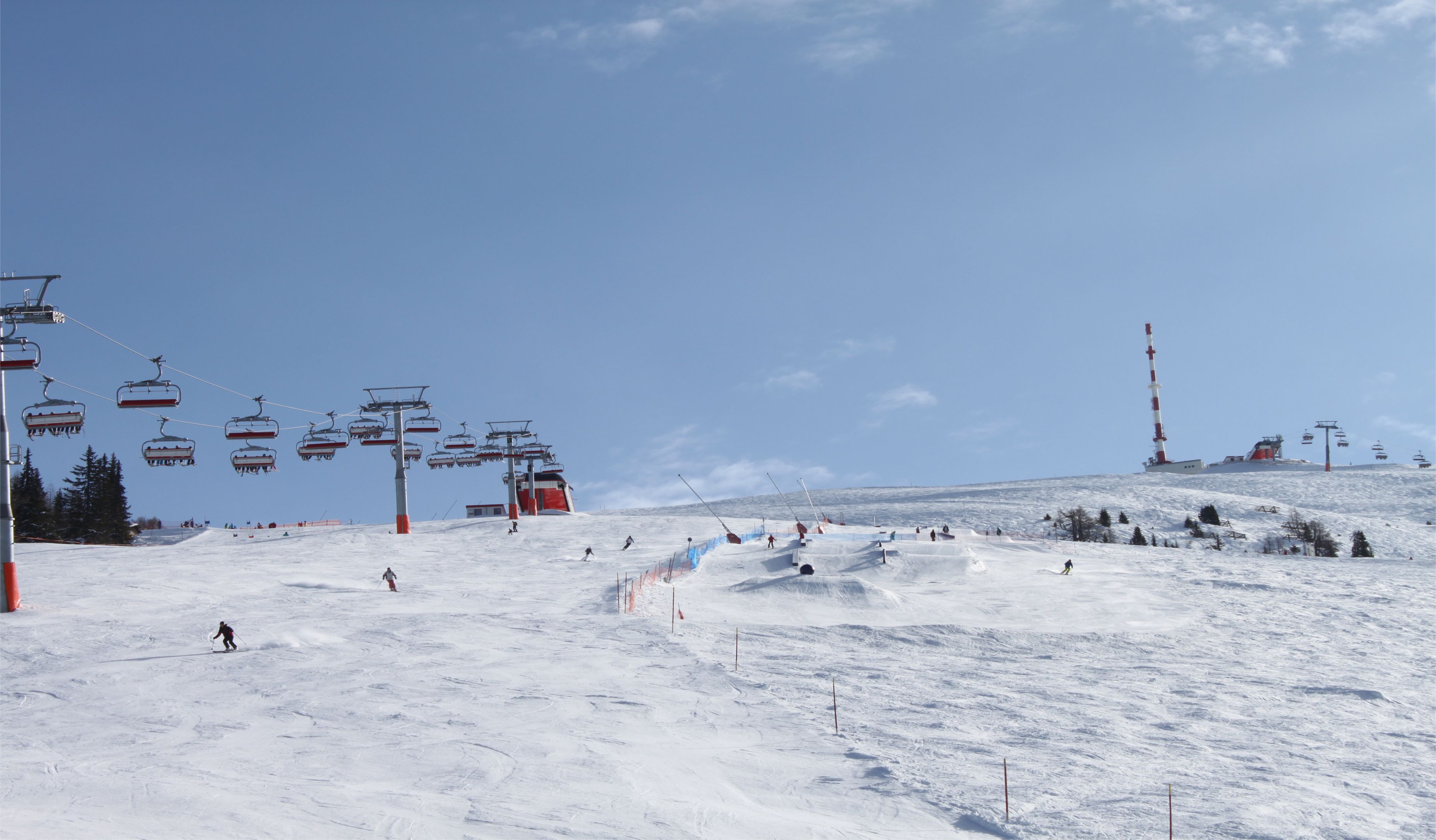 A ski slope with a ski lift and a tall red and white tower.