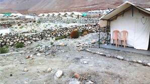 Entorno rústico al aire libre con un muro de piedra y una estructura parecida a una tienda, con sillas.