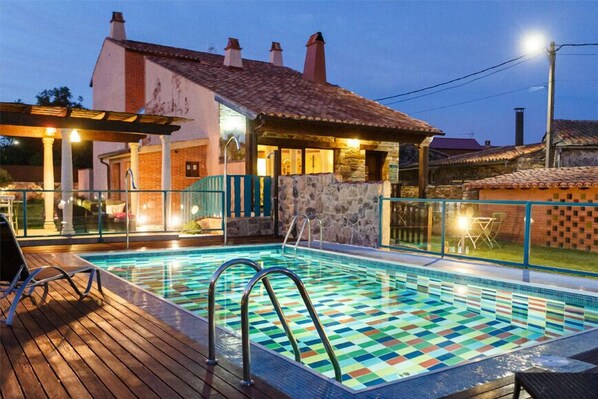 A swimming pool with a checkered tile pattern, surrounded by a wooden deck and stone walls.