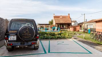 Casa rural con techo de tejas, zona ajardinada y un vehículo estacionado con matrícula visible.