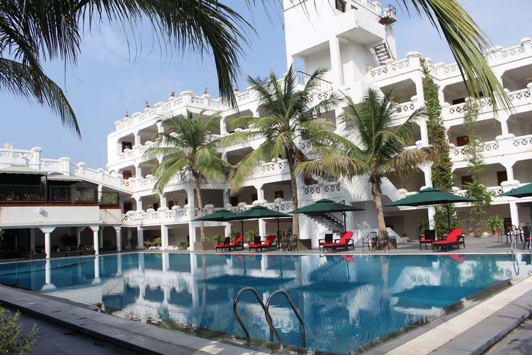 A hotel with a swimming pool surrounded by palm trees and red lounge chairs.