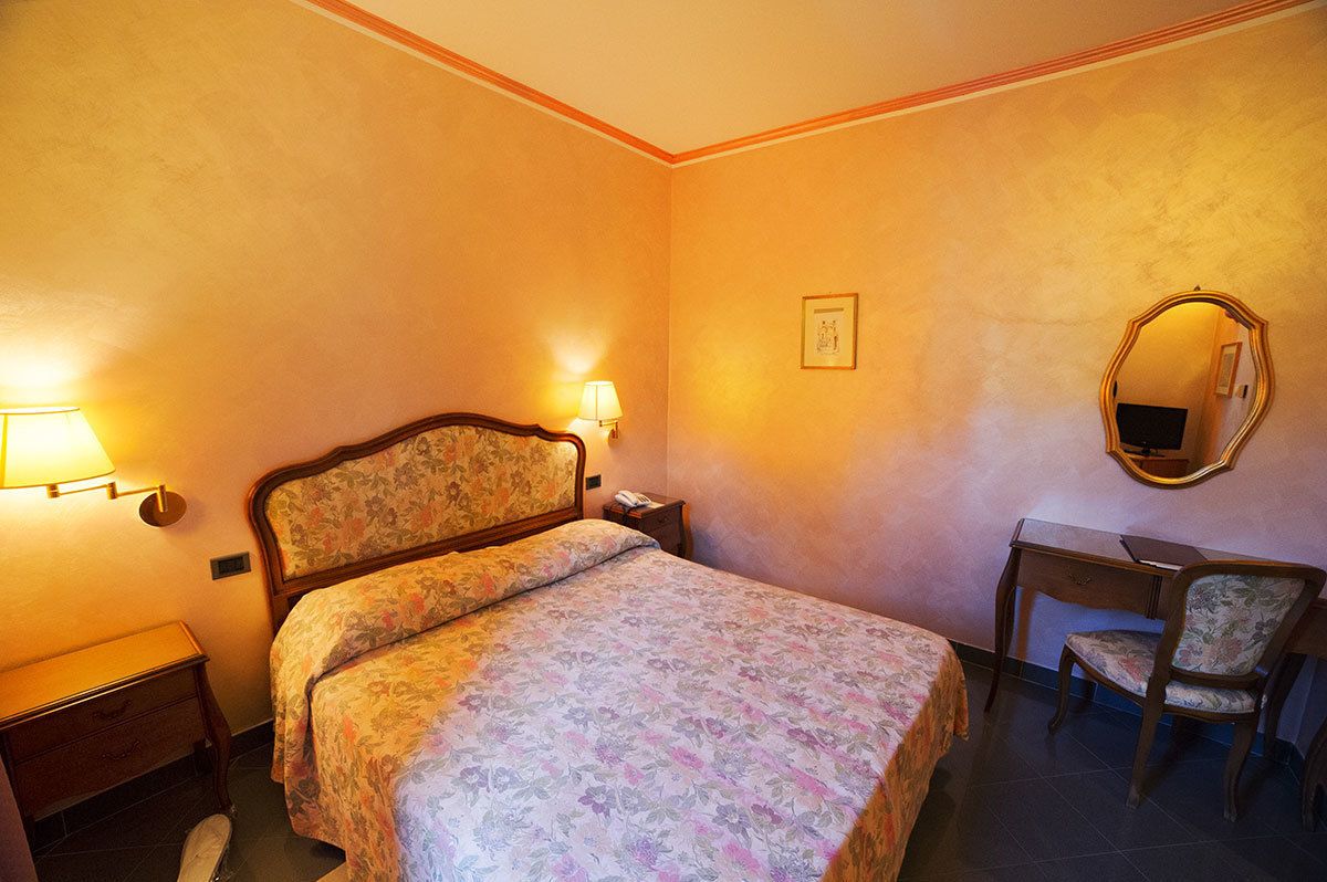 A bedroom with a bed, bedside table, lamp, desk, chair, and a mirror.