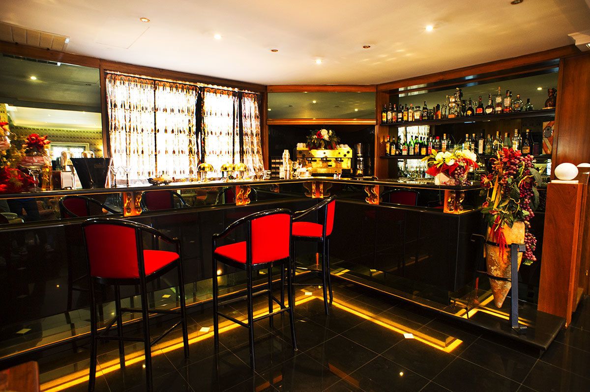 Una zona de bar con mostrador, taburetes rojos y estantería con botellas.