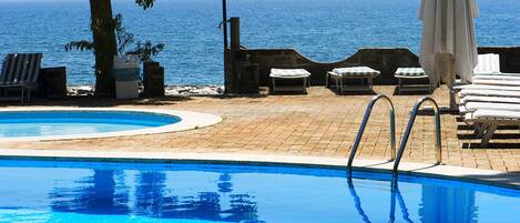 A pool area with lounge chairs and a view of the sea.