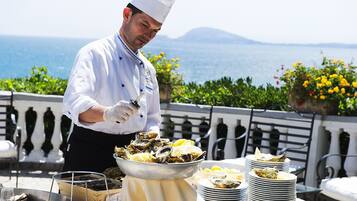 Ein Koch bereitet Austern mit Zitronenspalten auf einer Terrasse mit Meerblick zu.