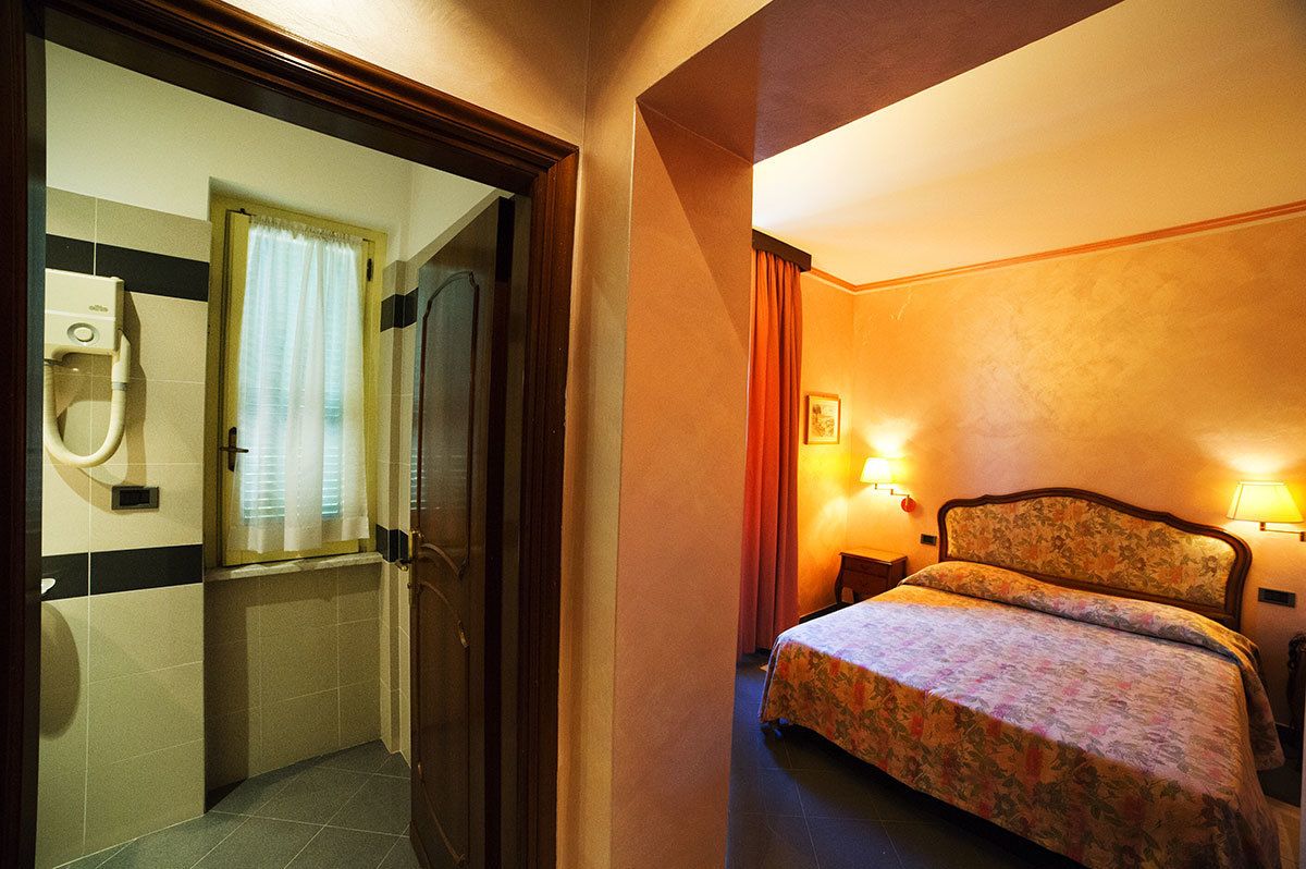 Een hotelkamer met een bed, nachtkastje, lamp en een badkamer met toilet en wastafel.