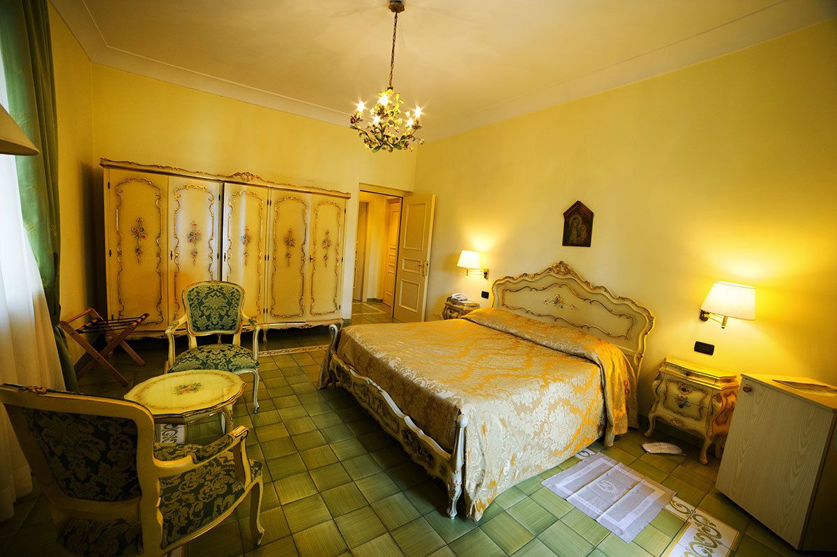 A room with a large bed, two chairs, a small table, a cabinet, and a chandelier.