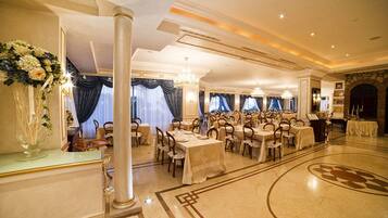A banquet hall with round tables, chandeliers, and a marble floor.