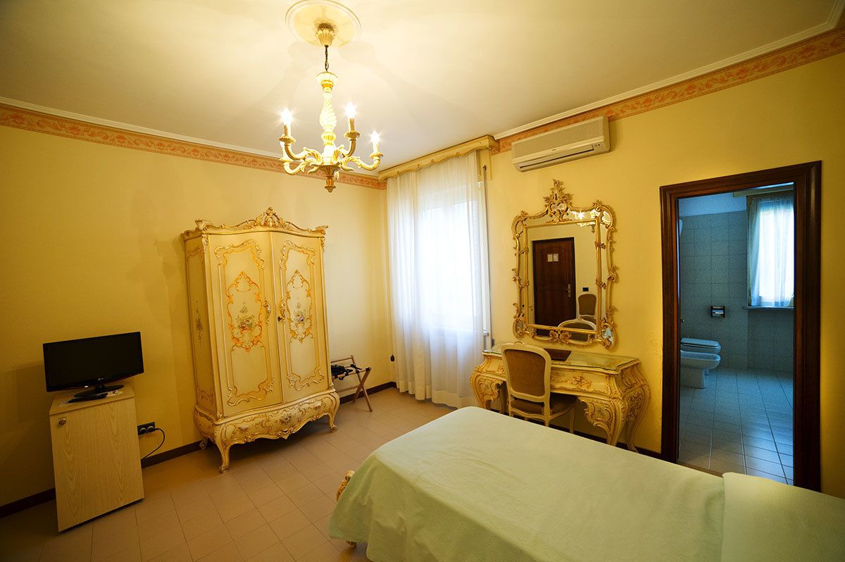 A hotel room with a bed, a desk, a television, an ornate wardrobe, and a mirror.