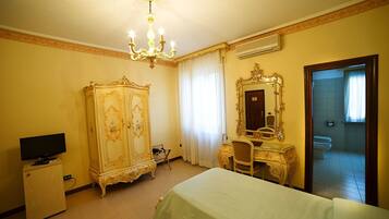 A hotel room with a bed, a desk, a television, an ornate wardrobe, and a mirror.