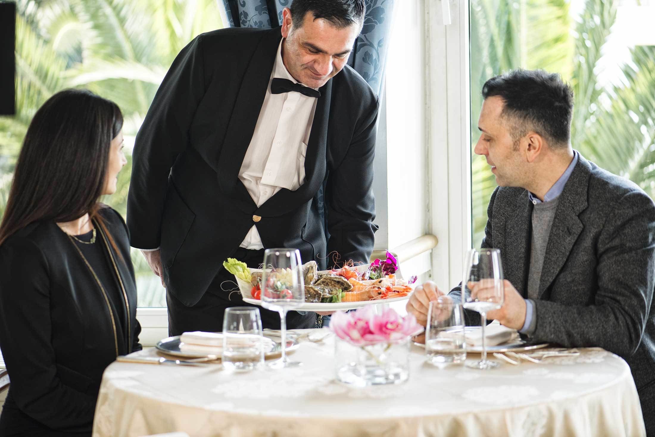 Une salle à manger élégante où un serveur apporte les plats aux convives à table.