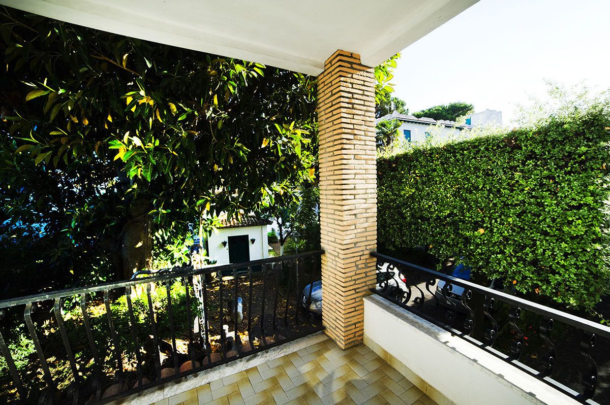A balcony with a tiled floor, a brick pillar, and a black metal railing.