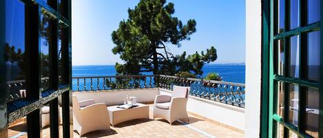 A balcony with outdoor furniture, a view of the sea, and a tree.