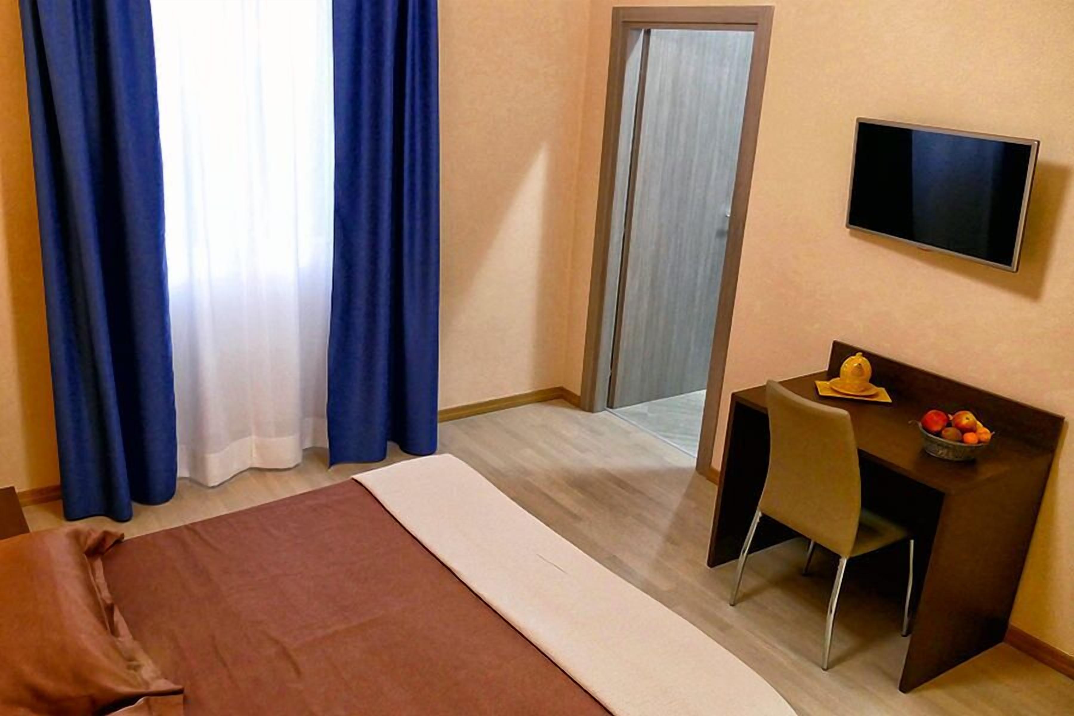 Ein Hotelzimmer mit einem Bett, einem Schreibtisch mit Stuhl, einem Fernseher und einem kleinen Tisch mit Obst.