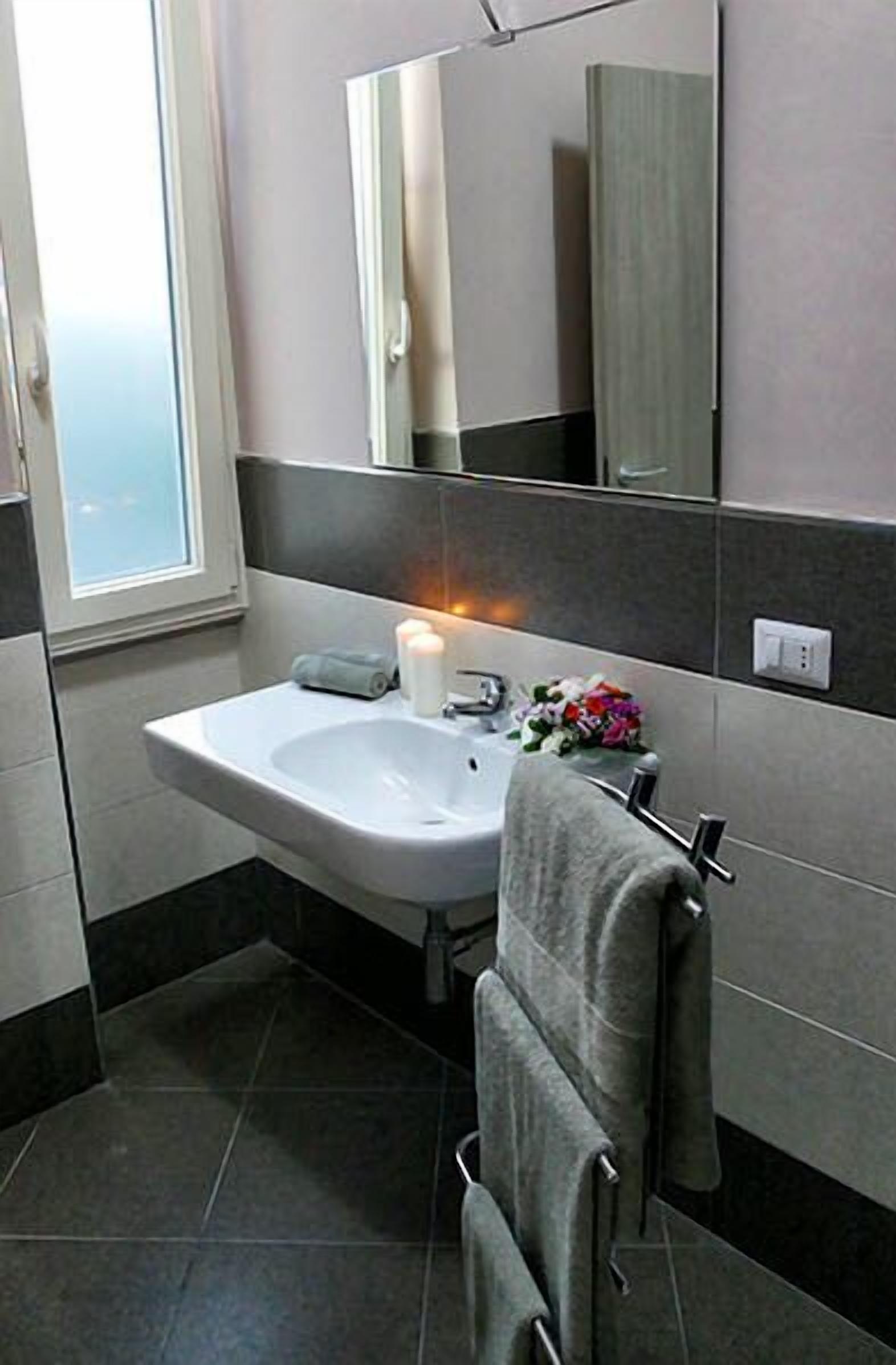 Une salle de bain avec un lavabo blanc, un miroir, un porte-serviettes et une fenêtre.